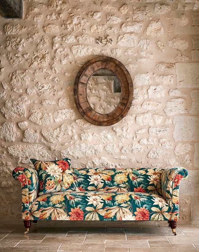 Green and red floral fabric on sofa with exposed brick backdrop